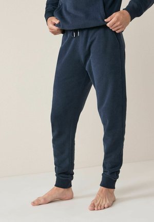 Pantalones de chándal azul marino con cintura ajustable por cordón, diseño de pierna entallada y puños de canalé. Hechos de un material suave y texturizado.