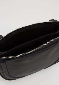 Borsa a tracolla in vera pelle nera con una texture liscia, dotata di chiusura con zip e due scomparti interni per un'organizzazione ottimale.