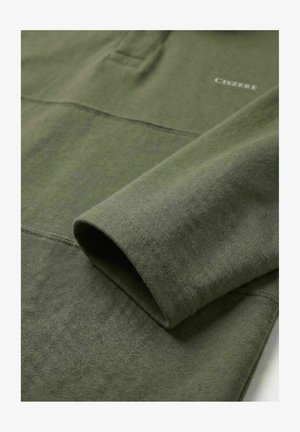 Olivengrønn langermet skjorte med synlige sømmer og liten hvit tekst «CISZBEE» nær skulderområdet.