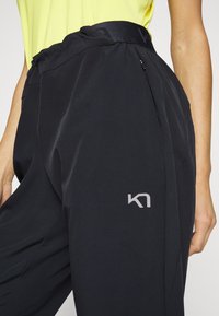 Svarta träningsbyxor med resårmidja och en liten grå logotyp på sidan. Slät, lättviktsmaterial.