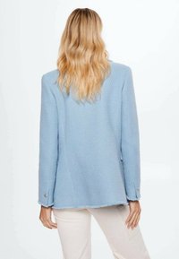 Světle modrý texturovaný blazer s mírně potrhanými lemy a knoflíkovými manžetami. Jednoduchý, dobře padnoucí design s čistým zadním pohledem.