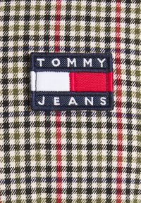 Naszywka z logo Tommy Jeans z białymi, czerwonymi i granatowymi paskami na tle tkaniny w zieloną, czarną i czerwoną kratę.