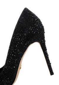 Talons aiguilles noirs avec un bout pointu, recouverts de cristaux noirs, dotés d'une semelle intérieure beige et d'un accent en métal doré près du talon.