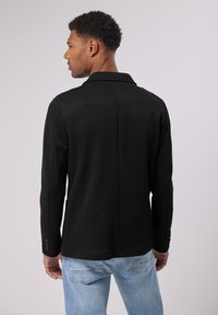 Černý blazer s hladkou texturou, přizpůsobeným střihem a klopovým límcem. Obsahuje knoflíky na manžetách a čistý šev na zadní straně.