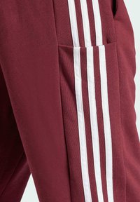 Bordo sporta bikses ar trim baltām vertikālām svītrām sānos un sānu kabatu ar teksturētu audumu.