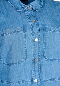 Denim-paita, joka on valmistettu vaaleansinisest�ä kankaasta, jossa on kaulus ja nepparit. Rinnassa on näkyvissä kaksi taskua, joiden pinnassa on sileä rakenne ja ompeluyksityiskohtia.