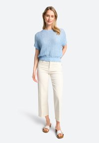 Lichtblauwe gebreide trui met korte mouwen, beige wijde strakke broek en witte instapsandalen. Zachte textuur en een ontspannen pasvorm.