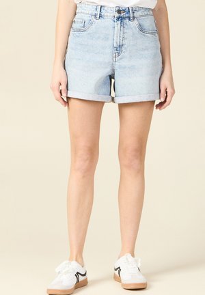 Shorts en denim bleu clair avec des ourlets retroussés, taille haute et poches avant. Associés à des baskets blanches avec des accents noirs.
