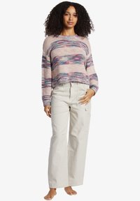 Maglione lavorato a maglia in colori pastello con un design cropped e orli a coste, abbinato a pantaloni cargo beige a gamba larga con molteplici tasche.