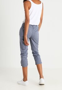 Grijze cropped broek van katoen met een gladde textuur, voorzien van een aansluitend ontwerp en achterzakken. Gecombineerd met witte sneakers.