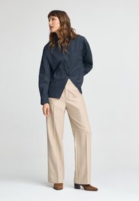 Granatowa koszula w paski zapinana na guziki o luźnym kroju, zestawiona z beżowymi spodniami na wysokim stanie o szerokich nogawkach oraz brązowymi botkami na obcasie.