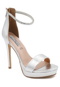 Sandal con tacco alto in metallo argentato, con cinturino alla caviglia, punta aperta, ampia fascia frontale e base con plateau per un'altezza aggiuntiva. Fettuccia con texture decorativa.