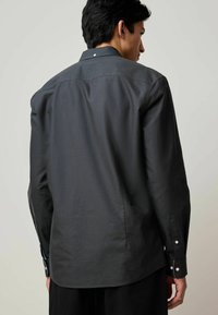Camisa negra de manga larga hecha de tejido suave, con cuello de punta, detalles de puños abotonados y un dobladillo recto en la parte posterior.