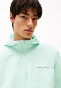 Mintgroene lichtgewicht hooded jas met een rits aan de voorkant, gaasvoering en het "TOMMY JEANS" logo geborduurd op de borst. Soepele textuur.