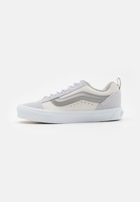 Graue und weiße Sneaker mit einem Obermaterial aus verschiedenen Materialien, das Wildlederakzente, einen klassischen Seitenstreifen und Perforationen für Atmungsaktivität aufweist.