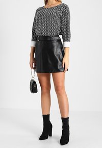 Svart och vit mönstrad topp med trekvartslånga ärmar, kombinerad med en svart läder minikjol och svarta klackstövlar. Liten svart handväska.