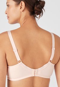 Reggiseno rosa chiaro con spalline regolabili, tessuto liscio e chiusura a gancio. Hardware minimale, design semplice e finitura senza cuciture.