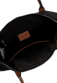 Interno di una borsa a mano in tessuto nero, con un'etichetta in pelle marrone, tasca con zip e una texture liscia con un accento di cucitura marrone.