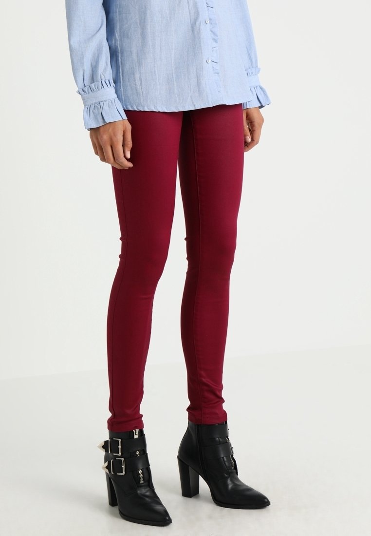 Jean skinny couleur marron foncé en mélange de coton, associé à une chemise bleu clair à boutons. Bottines noires à talons avec des accents de boucle.