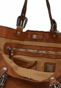 Sac fourre-tout en cuir avec un extérieur marron, des accessoires en métal, un compartiment principal avec une poche zippée et un revêtement en tissu.