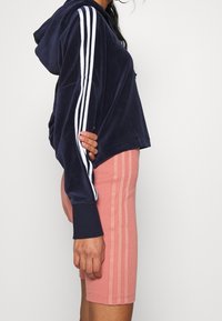 Marinblå sammet croppad hoodie med vita ränder på ärmarna, kombinerad med rosa ribbade cykelbyxor med två vertikala ränder.