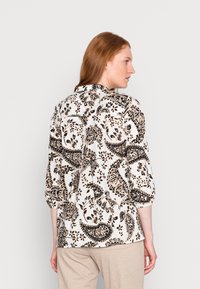 Blusa de mangas longas com um padrão de paisley preto em fundo creme; apresenta um colarinho clássico e mangas franzidas.