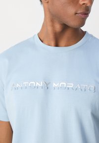 Lichtblauwe katoenen t-shirt met een ronde halslijn en glanzende zilveren letters "ANTONY MORATO" op de borst. Over het algemeen een gladde textuur.