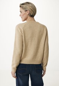 Beiger Wollpullover mit rundem Halsausschnitt und geripptem Saum, ausgestattet mit langen Ärmeln und einer weichen, strukturierten Oberfläche, kombiniert mit dunklen Jeans.