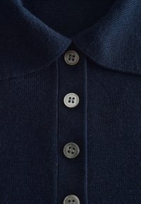 Vêtement tricoté bleu foncé avec un col plié et quatre boutons alignés verticalement au centre devant.