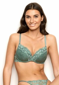 Pitkähihainen pitsi rintaliivi hillityssä vihreässä, jossa on syvä kaula-aukko, säädettävät olkaimet ja kukkakuviot. Pehmeä materiaali, jossa on kevyt topastus muodon tueksi.