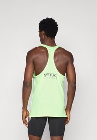 Mouwloze neonkleurige sporttanktop met meshstructuur, voorzien van "NEW YORK TOGETHER" in zwarte letters op de achterkant. Zwarte shorts gedragen.