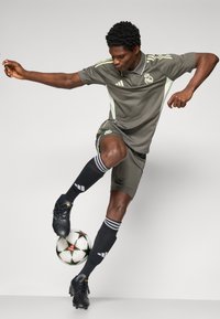 Mørkegrå fodbolduniform med hvide detaljer, sorte sokker og sorte fodboldstøvler. Spilleren balancerer en mønstrede fodbold på foden.