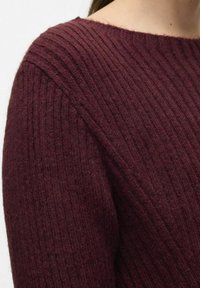 Maglione lavorato a maglia color bordeaux con texture a costine, scollo a barca e leggero svaso alle maniche, che enfatizza un aspetto accogliente e caldo.