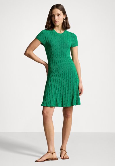 Vestido de punto verde con mangas cortas, textura de trenzado, busto ajustado, falda acampanada y dobladillo a medio muslo, combinado con sandalias marrones.