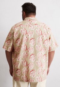 Korte mouwen overhemd in lichtbeige stof met een patroon van rode en witte tropische bladeren. Relaxte pasvorm met een uitgesneden kraag.