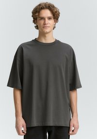 Tricou oversized gri închis, fabricat din bumbac moale, cu guler rotund și mâneci scurte. Textură netedă, design minim și fără modele vizibile.