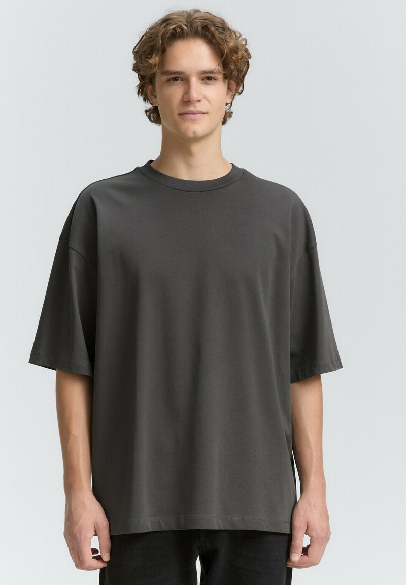 Tricou oversized gri închis, fabricat din bumbac moale, cu guler rotund și mâneci scurte. Textură netedă, design minim și fără modele vizibile.