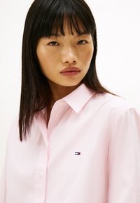 Světle růžová košile na knoflíky z bavlny s malým vyšívaným logem na hrudi. Košilový límec s hladkou texturou.