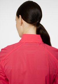 Rosa lättviktsjacka med hög krage. Slät textur och subtilt mönster, med en sportig design och axelsömsdetalj.