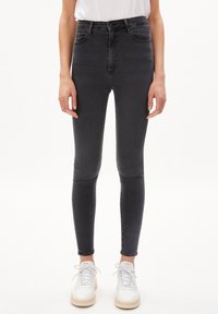 Černé skinny džíny s vysokým pasem vyrobené z denimu, s hladkou texturou a klasickým 5-kapanovým designem, doplněné bílými teniskami.
