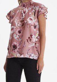Blusa floreale rosa con maniche corte a volant, scollo rotondo, caratterizzata da un mix di fiori grandi e piccoli in tonalità di viola e bianco.