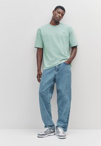 Mintgroen, T-shirt met korte mouwen en een ronde hals, gecombineerd met loszittende, vervaagde blauwe jeans en grijze sneakers met zwarte en witte accenten.