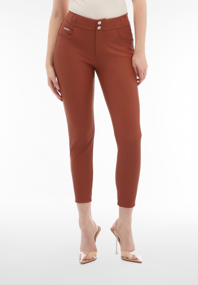 Pantalones de tiro alto de color óxido con textura suave, dos bolsillos frontales y cierre de doble botón. Ajustados hasta el tobillo, combinados con tacones transparentes.