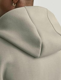 Felpa con cappuccio in cotone di colore grigio chiaro. Presenta una texture morbida, cuciture doppie e un cappuccio arrotondato con una finitura liscia.