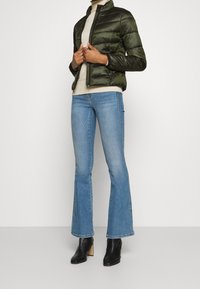 Puffjacka i mörkgrön, ribbad krage, dragkedja, tillsammans med ljusblå utsvängda jeans och svarta klackade ankelstövlar.