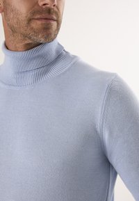 Lichtblauwe coltrui gemaakt van zachte gebreide stof. Heeft een geribbelde kraag en manchetten, een aansluitend ontwerp en een gladde textuur.
