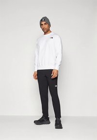Sweatshirt branco texturizado com um logótipo preto, combinado com calças pretas afuniladas com um pequeno logótipo, e um gorro cinzento em malha. Ténis pretos.