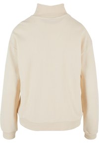 Sweat-shirt à manches longues couleur crème avec col roulé, poignets et ourlet côtelés, vu de dos sur un fond blanc.