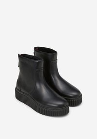 Bottines en cuir noir avec un bout rond, semelle en caoutchouc texturé et fermeture éclair sur le côté. Doublure douce visible au bord supérieur.