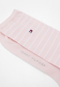 Rosa Baumwollsocke mit weißen vertikalen Streifen, die ein kleines gesticktes Logo in Rot, Weiß und Blau sowie grauen Markentext aufweist.